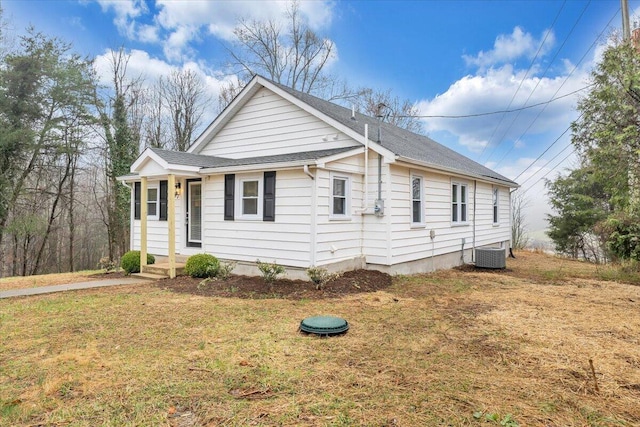 view of front facade with a front yard, central AC unit, and a shingled roof