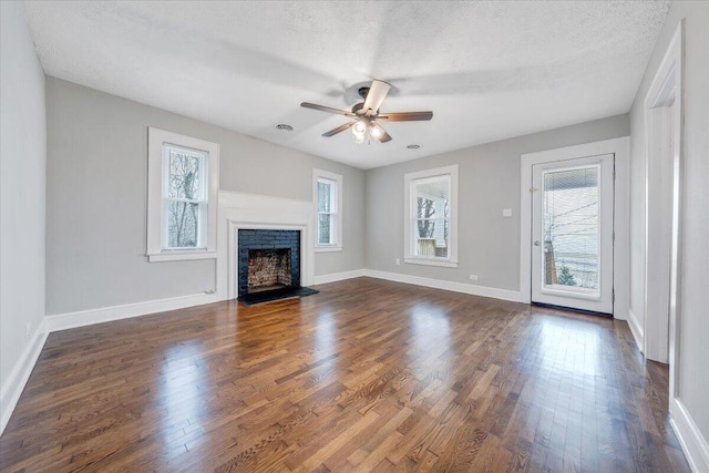 unfurnished living room with a ceiling fan, dark wood-style floors, baseboards, a fireplace with flush hearth, and a textured ceiling