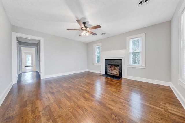 unfurnished living room with a fireplace with flush hearth, dark wood-style floors, visible vents, and baseboards