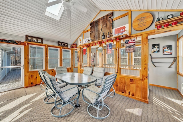 carpeted dining room featuring baseboards, lofted ceiling with skylight, ceiling fan, and wood walls