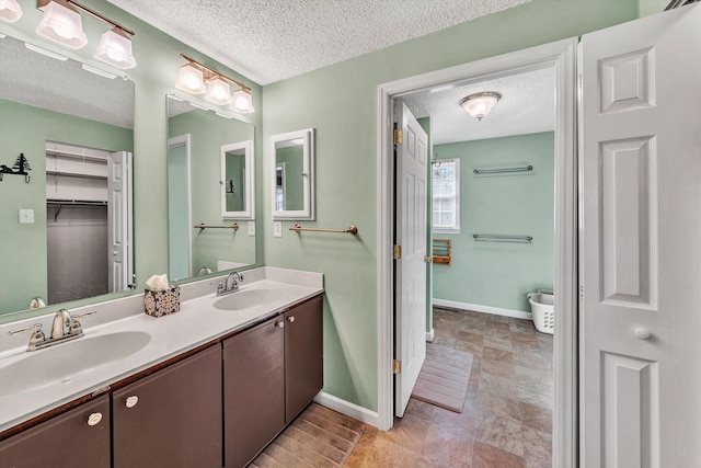 full bath featuring double vanity, a textured ceiling, baseboards, and a sink