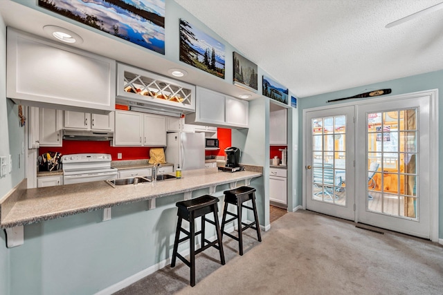 kitchen with under cabinet range hood, white appliances, a breakfast bar, and a sink