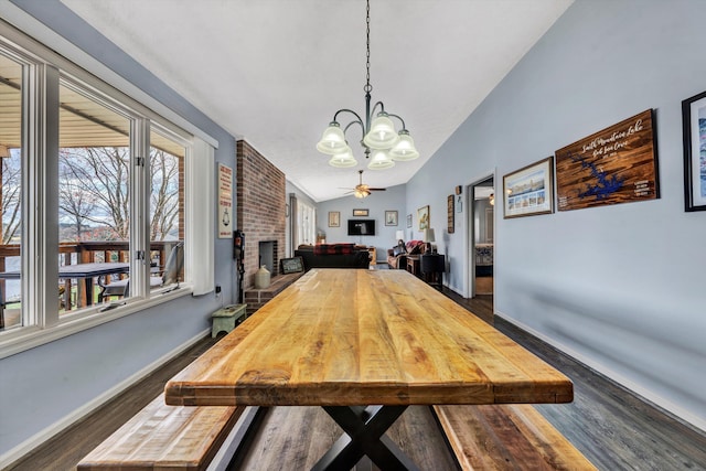 dining area featuring a brick fireplace, baseboards, dark wood finished floors, vaulted ceiling, and ceiling fan with notable chandelier