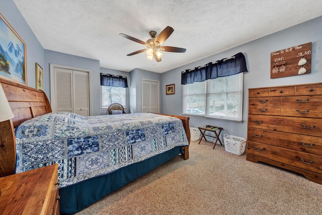 bedroom featuring ceiling fan, carpet, two closets, and a textured ceiling