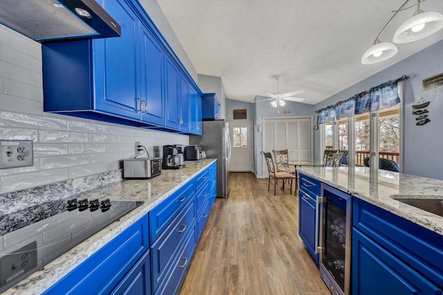 kitchen with beverage cooler, range hood, blue cabinetry, and freestanding refrigerator