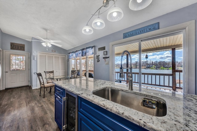 kitchen featuring blue cabinetry, light stone countertops, vaulted ceiling, dark wood-style floors, and a sink