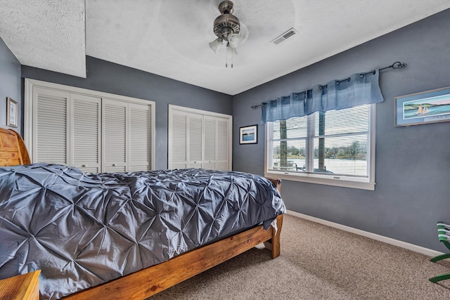 carpeted bedroom with baseboards, multiple closets, visible vents, and ceiling fan