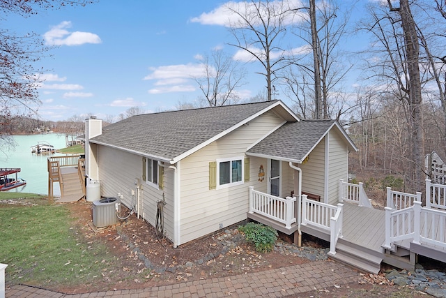 view of side of home featuring a deck with water view, central AC, a chimney, and a shingled roof