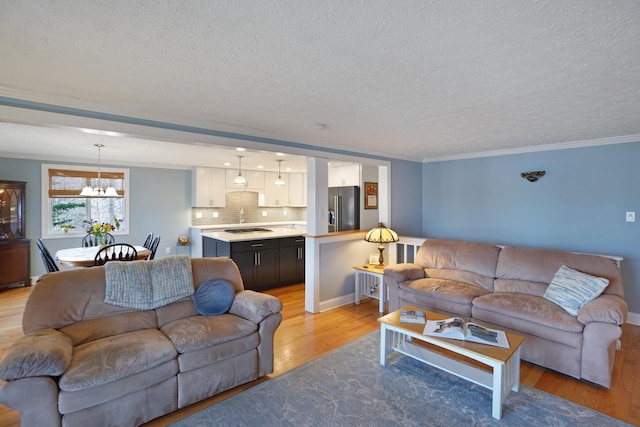 living room featuring an inviting chandelier, crown molding, light wood finished floors, and a textured ceiling