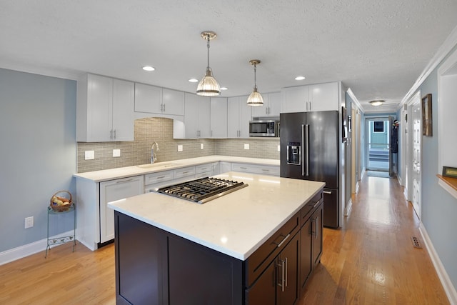 kitchen with light wood finished floors, tasteful backsplash, light countertops, stainless steel appliances, and a sink