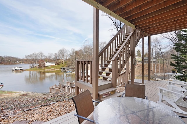 wooden deck featuring outdoor dining space, stairway, and a water view