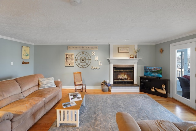 living room featuring baseboards, crown molding, a lit fireplace, and wood finished floors