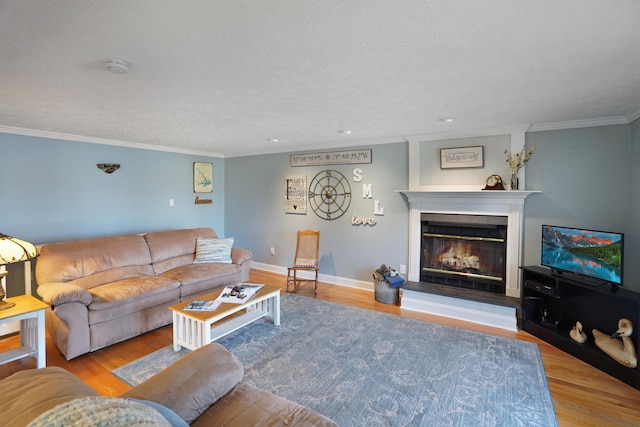 living room with wood finished floors, baseboards, a textured ceiling, a glass covered fireplace, and crown molding