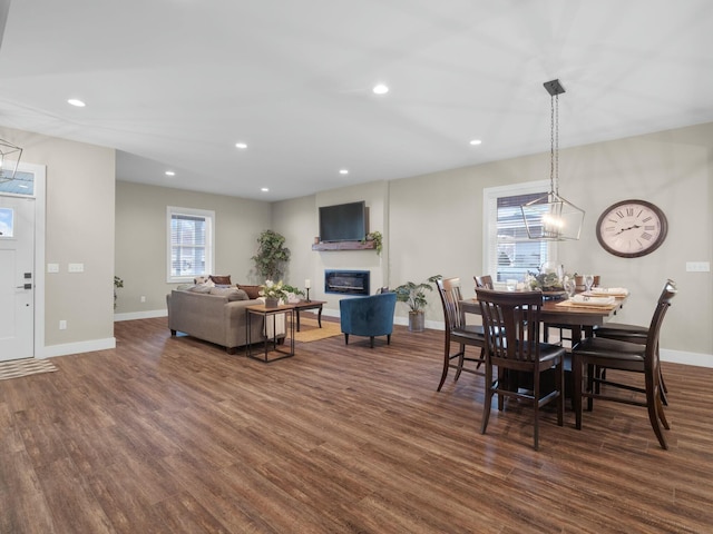 dining space featuring a glass covered fireplace, dark wood-type flooring, and baseboards