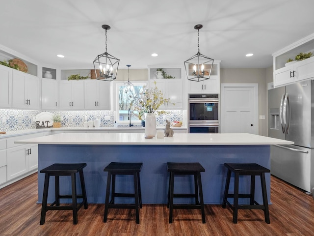 kitchen featuring a kitchen island, stainless steel appliances, light countertops, white cabinets, and a kitchen bar