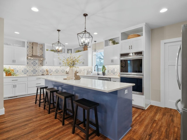 kitchen featuring dark wood finished floors, appliances with stainless steel finishes, a center island, and wall chimney range hood