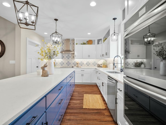 kitchen featuring dishwasher, wall chimney exhaust hood, blue cabinets, and a sink