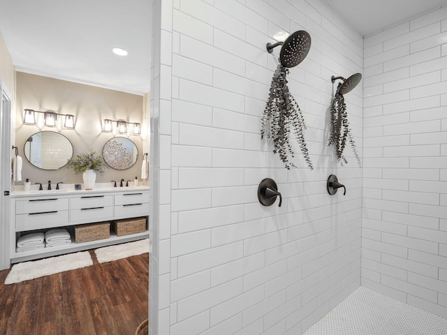 bathroom featuring double vanity, wood finished floors, tiled shower, and a sink