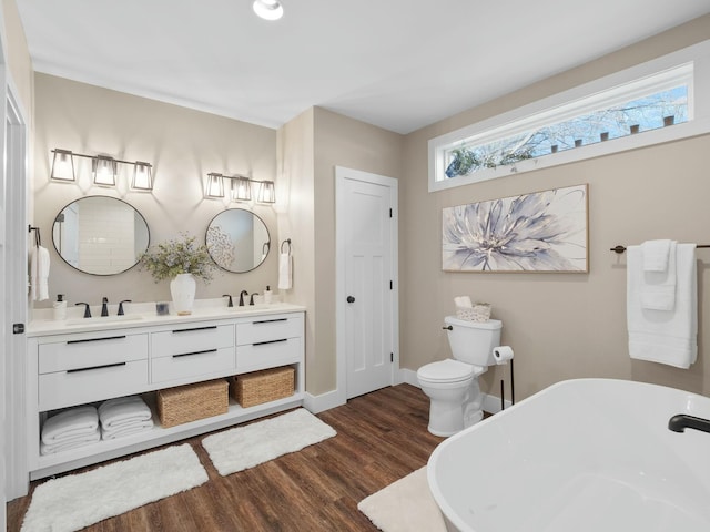 full bathroom featuring baseboards, a freestanding bath, double vanity, wood finished floors, and a sink