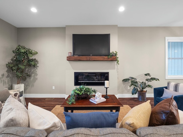 living room featuring a glass covered fireplace, recessed lighting, baseboards, and wood finished floors