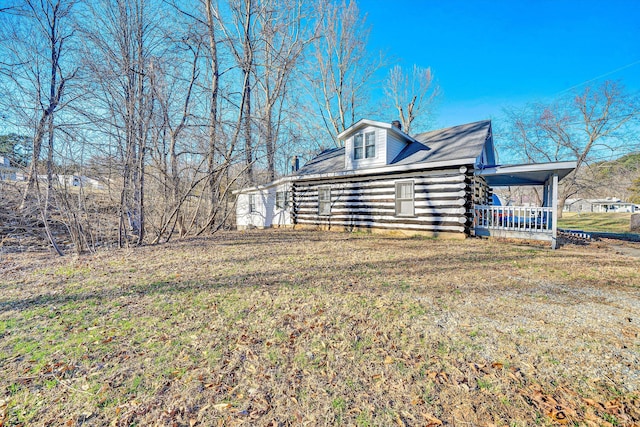 view of side of home with a porch, log exterior, and a yard