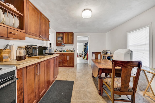 kitchen featuring light countertops, glass insert cabinets, range, and brown cabinetry