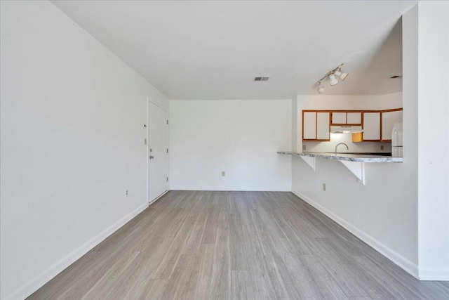 unfurnished living room with visible vents, light wood-type flooring, and baseboards