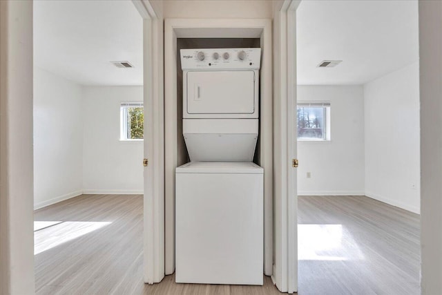 laundry room with a wealth of natural light, visible vents, and stacked washing maching and dryer