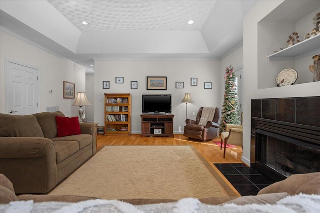 living area with visible vents, a tray ceiling, wood finished floors, a fireplace, and crown molding