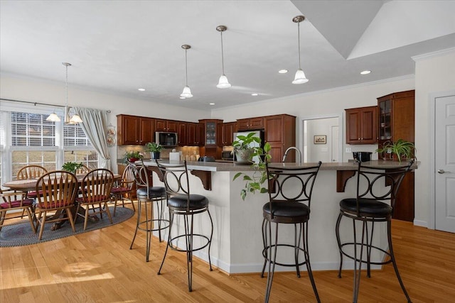 kitchen featuring light wood-style flooring, glass insert cabinets, crown molding, a kitchen bar, and stainless steel microwave