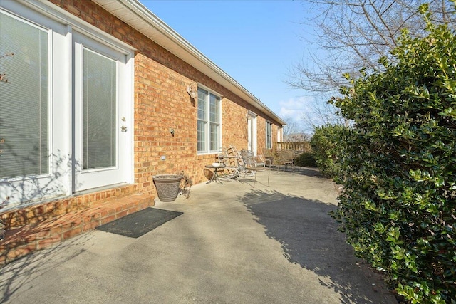 view of side of property featuring brick siding, a patio, and fence