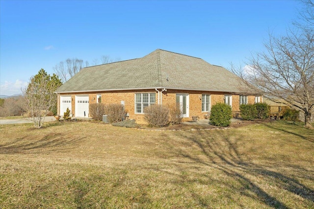 back of house with a yard, brick siding, a garage, and driveway