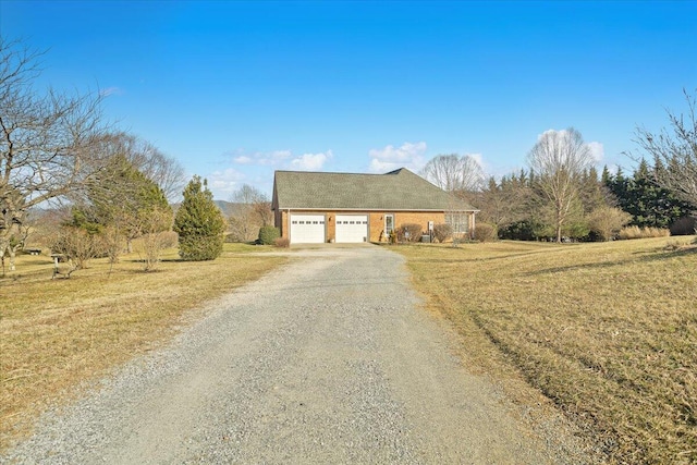 view of front of property featuring an attached garage, gravel driveway, and a front lawn