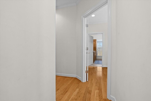 hallway featuring light wood finished floors, crown molding, and baseboards