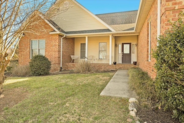 property entrance featuring brick siding, covered porch, a lawn, and a shingled roof