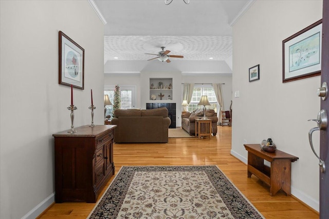 living room featuring crown molding, baseboards, light wood finished floors, and ceiling fan