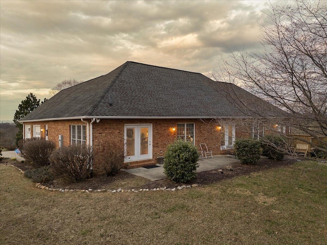 rear view of property featuring a yard, brick siding, roof with shingles, and a patio area