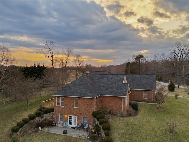 rear view of house featuring brick siding, a patio area, a lawn, and french doors