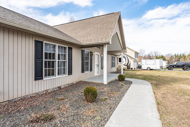 doorway to property with a lawn, roof with shingles, and a patio area