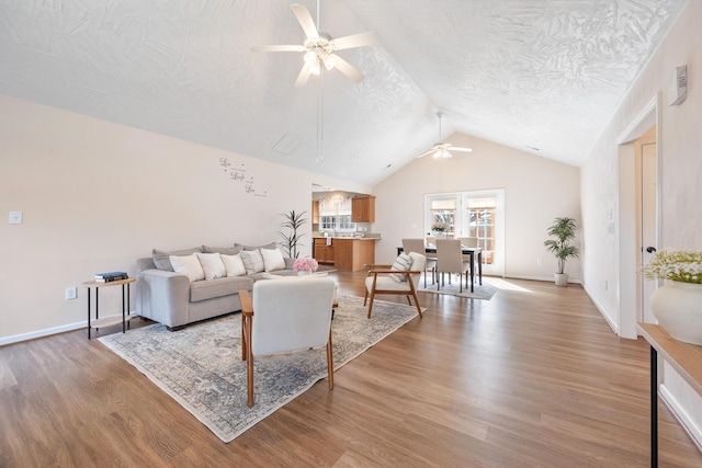 living room featuring lofted ceiling, a ceiling fan, a textured ceiling, light wood-style floors, and baseboards