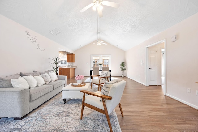 living room featuring vaulted ceiling, a ceiling fan, light wood-style floors, and a textured ceiling