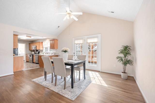 dining area with light wood-style flooring, baseboards, visible vents, and high vaulted ceiling