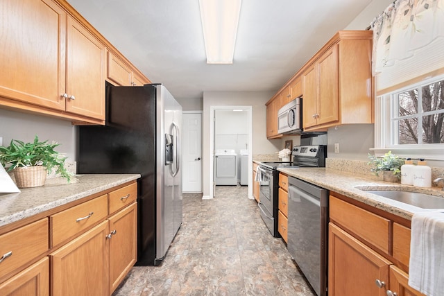 kitchen featuring light stone counters, a sink, stainless steel appliances, stone finish flooring, and washer and clothes dryer