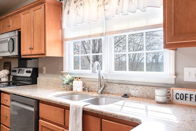 kitchen with a sink, stainless steel appliances, light stone countertops, and brown cabinetry