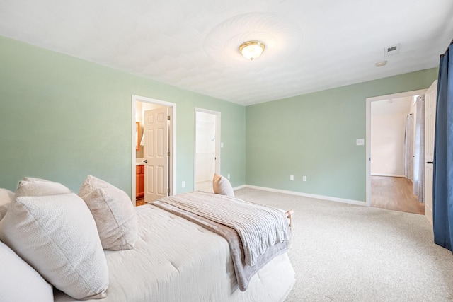 carpeted bedroom with visible vents, ensuite bathroom, and baseboards