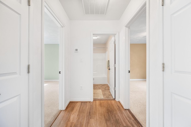 hallway featuring baseboards, visible vents, light wood finished floors, and light carpet