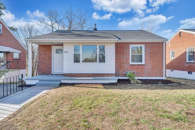 bungalow featuring brick siding, a shingled roof, a front lawn, and fence