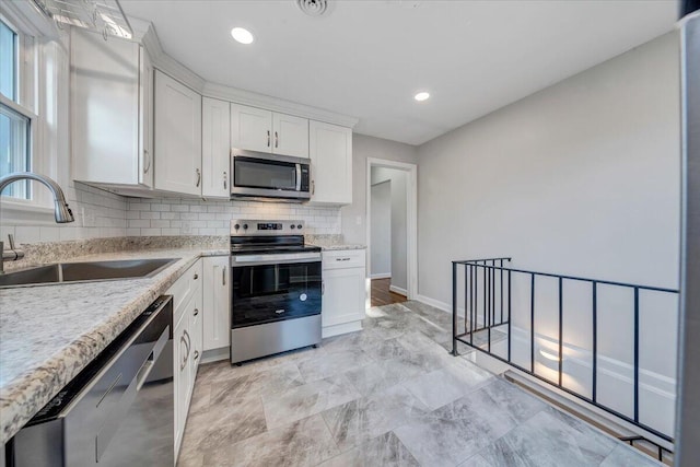 kitchen featuring light stone countertops, a sink, decorative backsplash, stainless steel appliances, and white cabinets