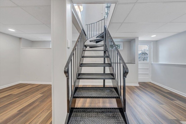 staircase featuring recessed lighting, a drop ceiling, baseboards, and wood finished floors