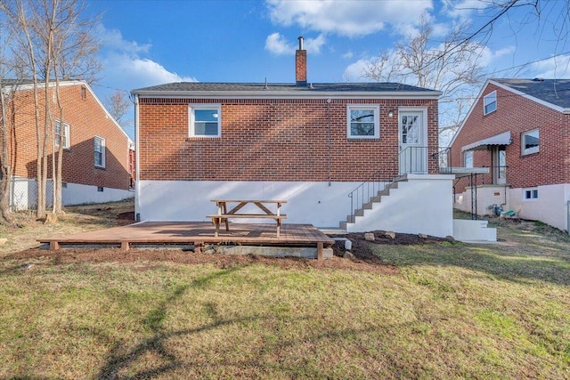 rear view of property featuring brick siding, a deck, a chimney, and a yard